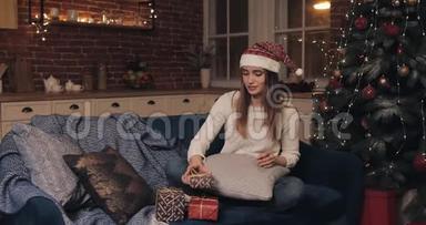 戴着圣诞帽的漂亮女孩坐在沙发上，靠近圣诞树，最后完成圣诞礼物的打<strong>包带</strong>